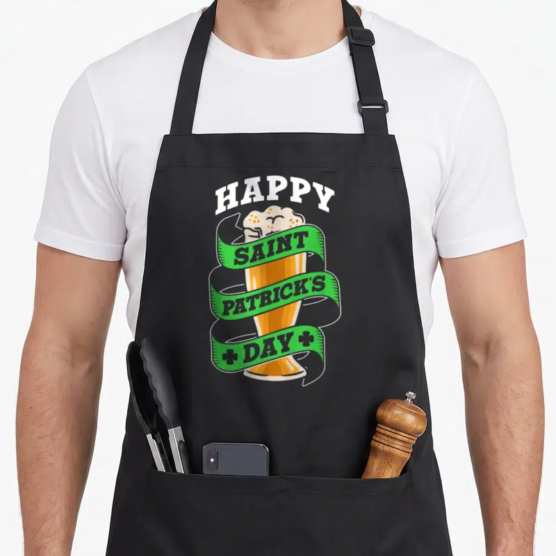 Tablier de cuisine noir avec illustration de bière et ruban vert portant l'inscription Happy Saint Patrick's Day.