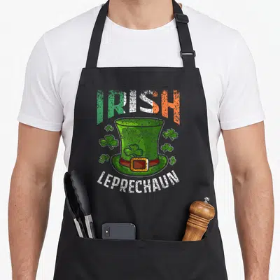Tablier de cuisine noir avec un chapeau de leprechaun vert, des trèfles et les mots Irish Leprechaun imprimés en style délavé.