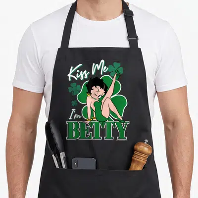 Tablier de cuisine noir avec Betty Boop en robe verte posant sur le mot BETTY entouré de trèfles.