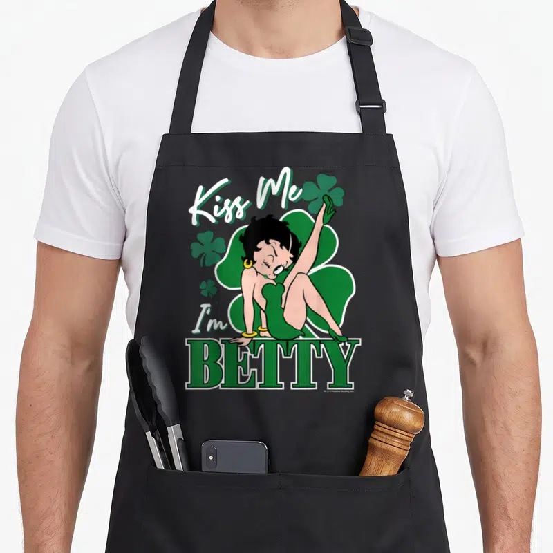Tablier de cuisine noir avec Betty Boop en robe verte posant sur le mot BETTY entouré de trèfles.