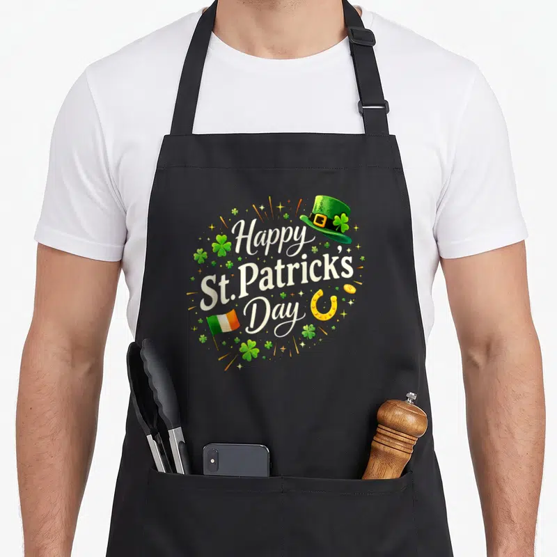 Tablier de cuisine noir avec inscription Happy St Patrick's Day entourée de trèfles et d'un chapeau vert.
