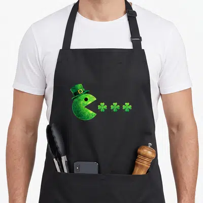 Tablier de cuisine noir avec pacman vert chapeau leprechaun dévorant trois trèfles à quatre feuilles alignés.