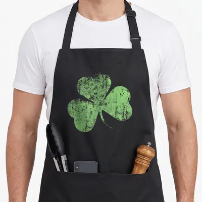 Tablier de cuisine noir avec un grand trèfle vert à l'aspect vieilli et texturé au centre du panneau avant.