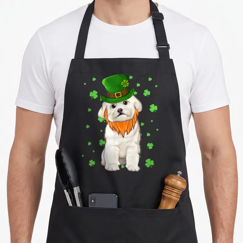 Tablier de cuisine noir avec chien blanc coiffé d'un chapeau vert et d'une barbe orange parmi des trèfles verts.