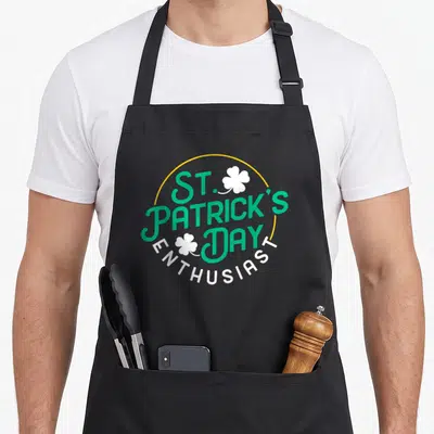 Tablier de cuisine noir avec inscription St Patrick Day Enthusiast et motifs de trèfles verts et blancs.