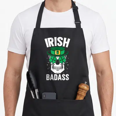 Tablier de cuisine noir avec un crâne portant un chapeau vert et des trèfles comme lunettes.