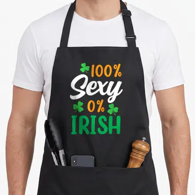 Tablier de cuisine noir avec l'inscription 100 % Sexy 0 % Irish et des trèfles verts et oranges.