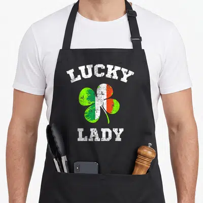 Tablier de cuisine noir avec un trèfle aux couleurs irlandaises et le texte Lucky Lady en blanc.