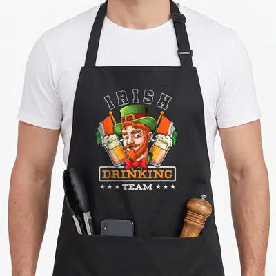 Tablier de cuisine noir avec illustration colorée d'un leprechaun tenant deux verres de bière et le texte IRISH DRINKING TEAM.