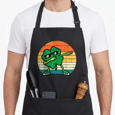 Tablier de cuisine noir avec un trèfle vert effectuant le dabbing sur fond rétro coloré.