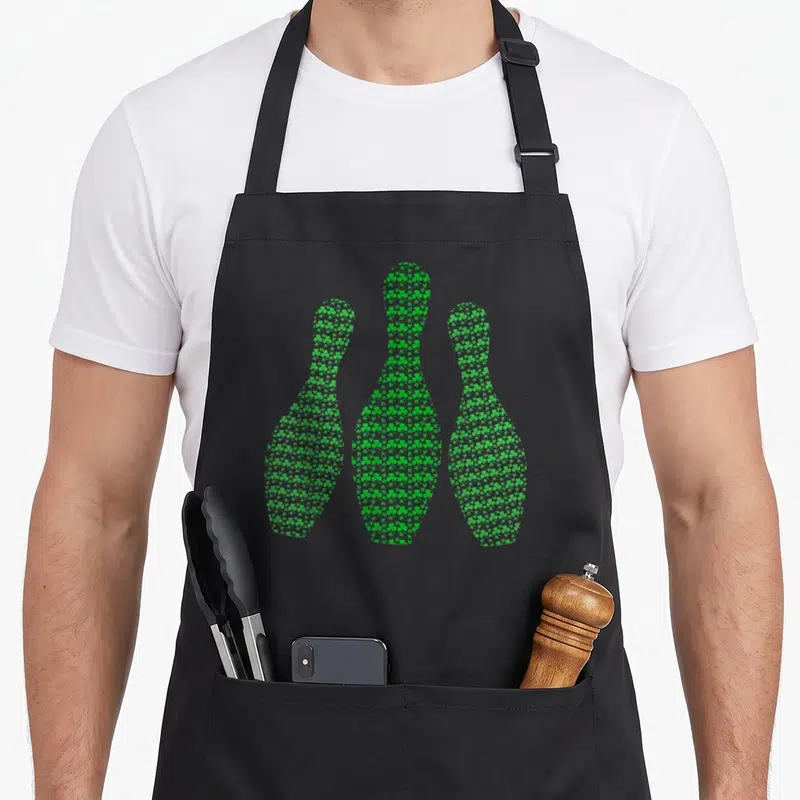 Tablier de cuisine noir avec trois quilles de bowling composées de petits trèfles verts imprimés sur le devant.