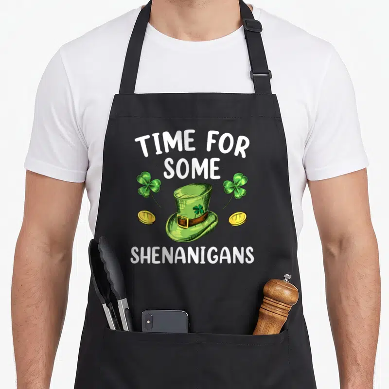 Tablier de cuisine noir avec illustration d'un chapeau de lutin vert, des trèfles et le texte Time For Some Shenanigans.