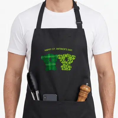 Tablier de cuisine noir avec deux ours stylisés en kilt et trèfles verts sous le texte Happy St. Patrick's Day.
