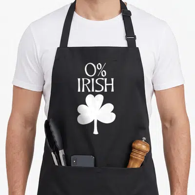 Tablier de cuisine noir avec inscription 0% IRISH et illustration de trèfle à trois feuilles en blanc.