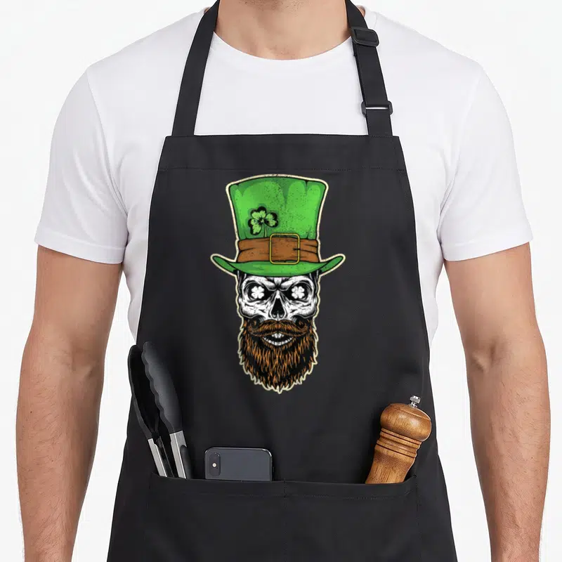 Tablier de cuisine noir avec illustration d'un crâne de lutin barbu coiffé d'un chapeau vert orné d'un trèfle.
