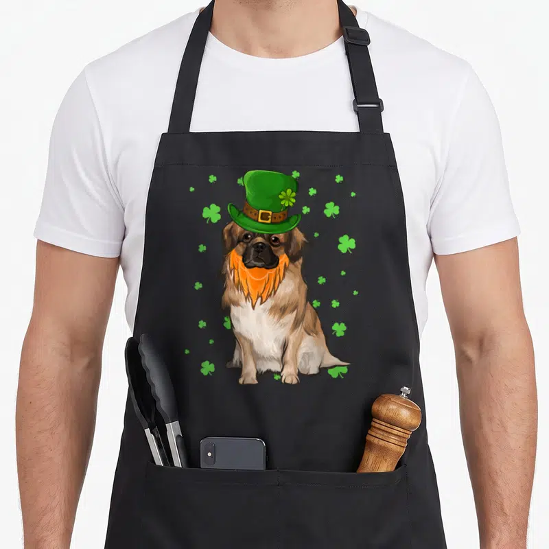Tablier de cuisine noir avec un epagneul tibetain portant un chapeau vert et des trèfles verts en arrière-plan.