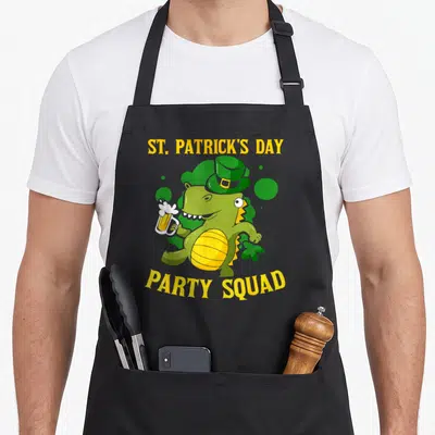 Tablier de cuisine noir avec un crocodile vert portant un chapeau et tenant une bière sous les textes St Patrick's Day et Party Squad.