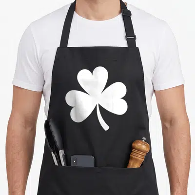 Tablier de cuisine noir avec un grand shamrock blanc stylisé au centre du torse.