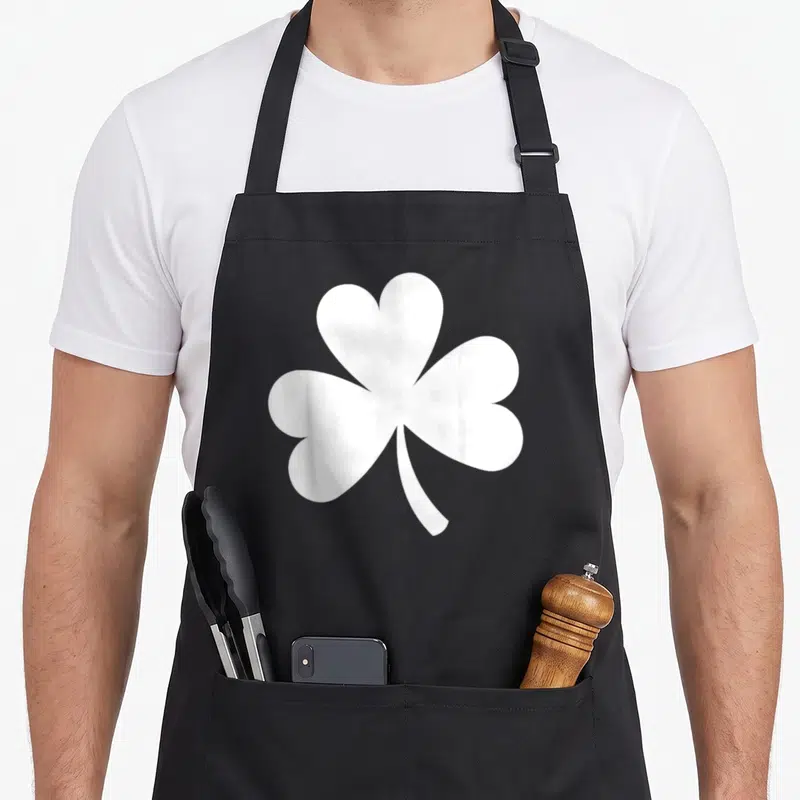 Tablier de cuisine noir avec un grand shamrock blanc stylisé au centre du torse.