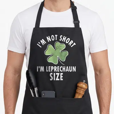 Tablier de cuisine noir avec un grand trèfle vert et le texte blanc I'm Not Short I'm Leprechaun Size au centre.