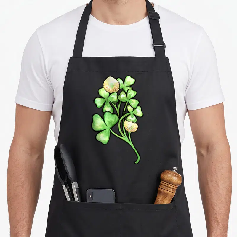 Tablier de cuisine noir avec illustration de trèfles verts et fleurs blanches au style aquarelle néerlandais.