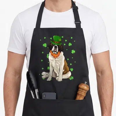 Tablier de cuisine noir avec illustration d'un chien St Bernard coiffé d'un chapeau vert à trèfle, entouré de motifs de trèfles verts.