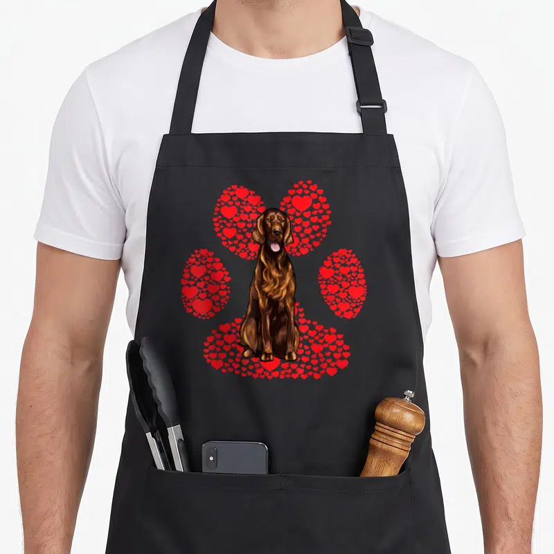 Tablier de cuisine noir avec illustration d'un setter irlandais assis devant une patte canine composée de petits cœurs rouges vifs.