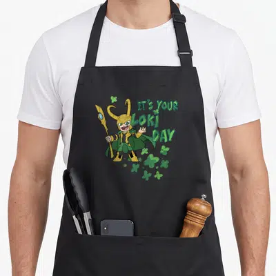 Tablier de cuisine noir avec Loki chibi tenant une lance, texte vert et trèfles à quatre feuilles.