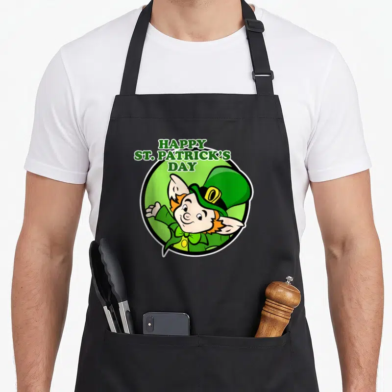 Tablier de cuisine noir avec un lutin aux cheveux roux et un chapeau vert, entouré du texte Happy St Patrick's Day.