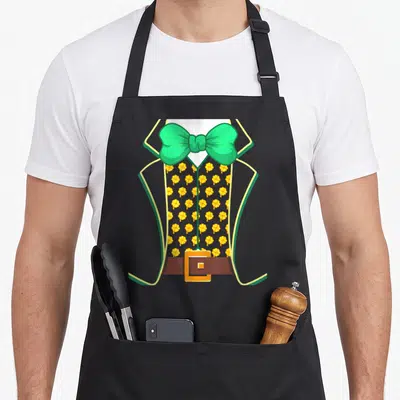 Tablier de cuisine noir avec illustration de costume de lutin, nœud papillon vert et motifs de trèfles jaunes sur le gilet.