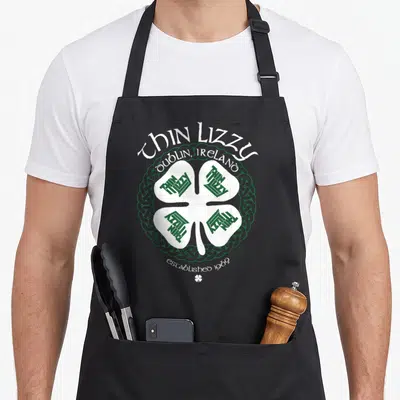 Tablier de cuisine noir avec un grand trèfle blanc et des nœuds celtiques verts portant les mots Thin Lizzy Dublin Ireland established 1969.