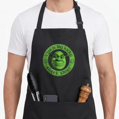 Tablier de cuisine noir avec le visage de Shrek vert dans un cercle orné de trèfles.