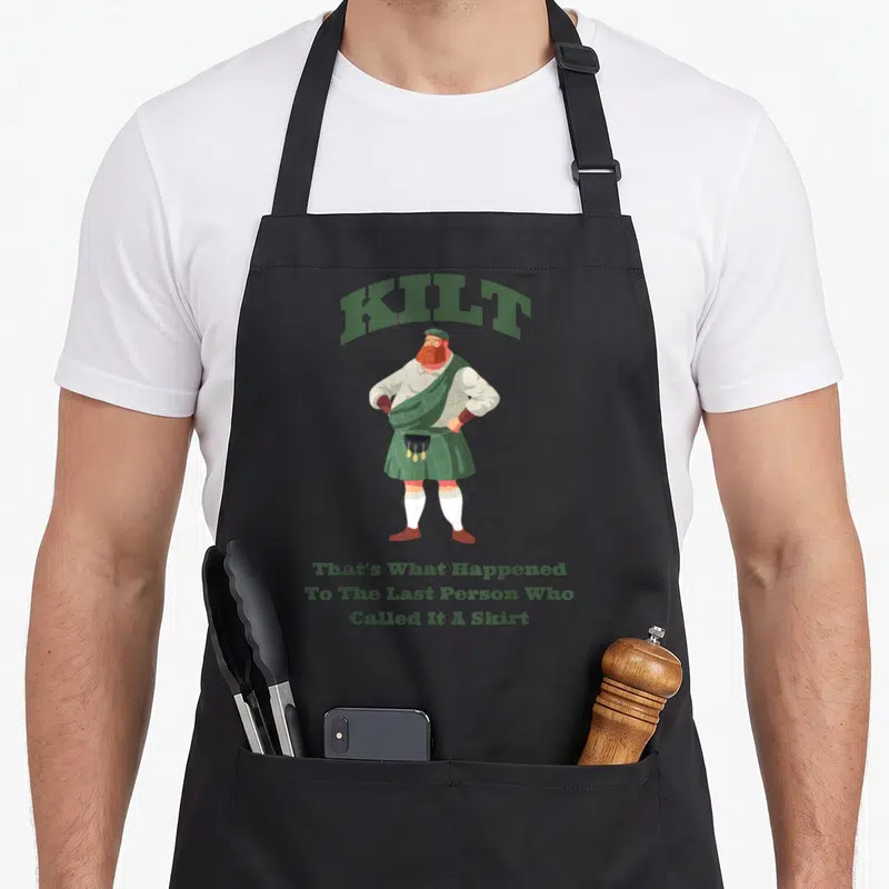 Tablier de cuisine noir avec illustration d'un homme en kilt vert et texte humoristique en anglais.