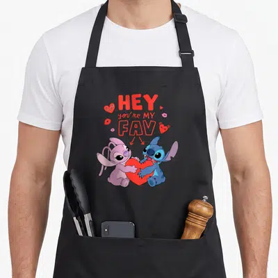 Tablier de cuisine noir avec Stitch et Angel tenant un grand cœur rouge sous le texte Hey you're my fav love.