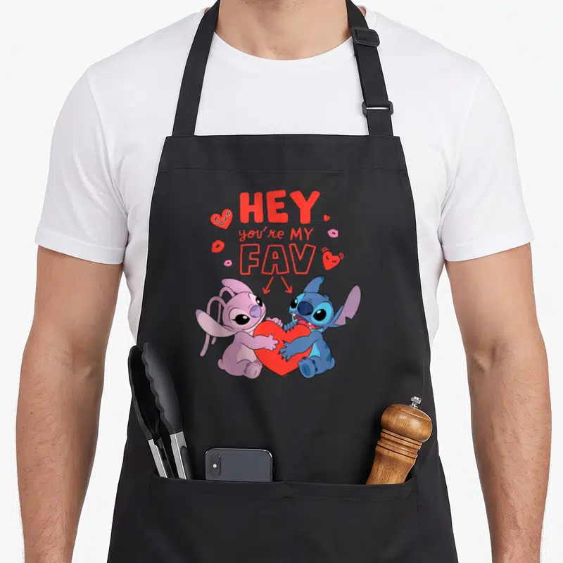 Tablier de cuisine noir avec Stitch et Angel tenant un grand cœur rouge sous le texte Hey you're my fav love.