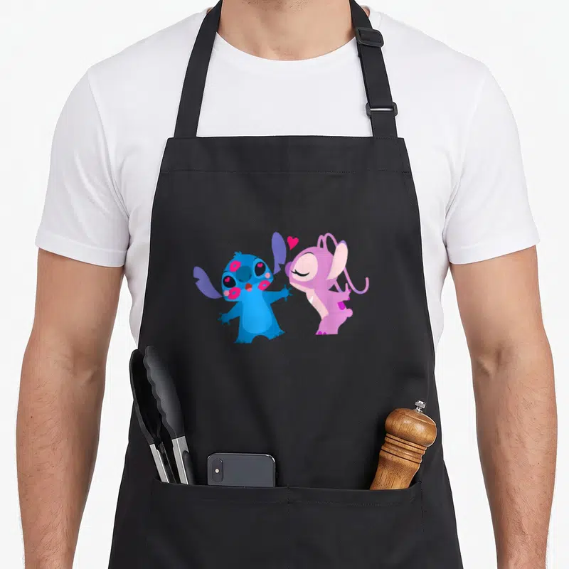 Tablier de cuisine noir avec Stitch bleu couvert de baisers roses et Angel rose qui lui envoie un cœur rouge sur le devant.