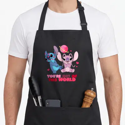 Tablier de cuisine noir avec Stitch bleu, Angel rose et l'inscription You're Out of This World sur fond uni.