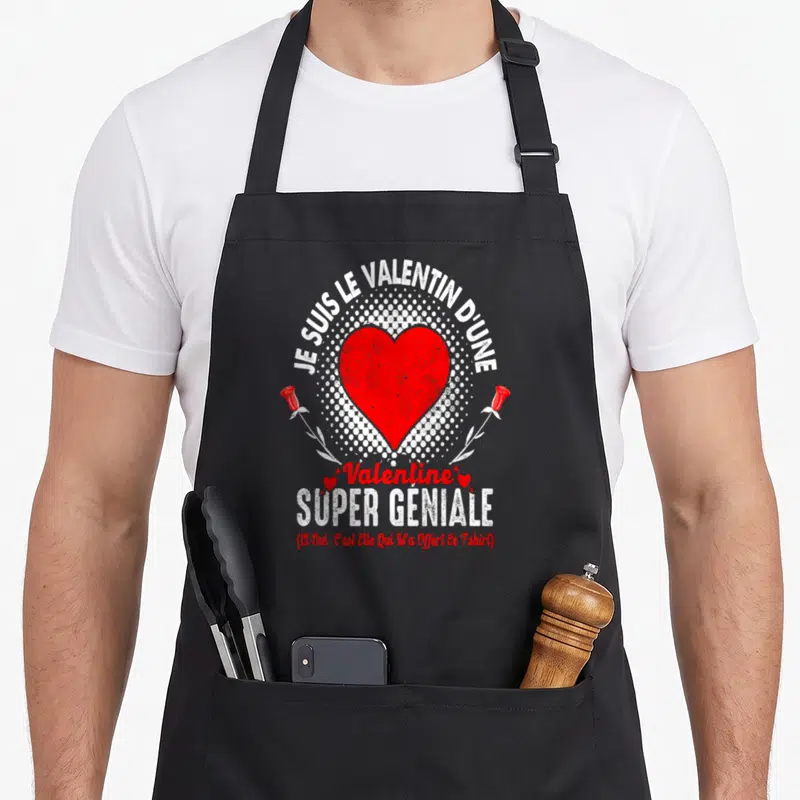 Tablier de cuisine noir avec un grand cœur rouge, des roses blanches et le texte Je suis le valentin d'une Valentine super géniale