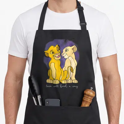 Tablier de cuisine noir avec deux lionceaux dorés se regardant tendrement devant un fond violet étoilé et une inscription blanche en bas.