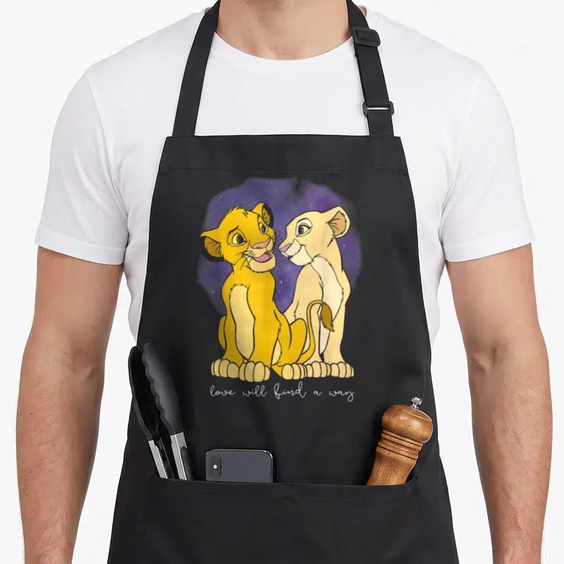 Tablier de cuisine noir avec deux lionceaux dorés se regardant tendrement devant un fond violet étoilé et une inscription blanche en bas.