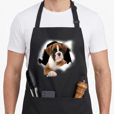 Tablier de cuisine noir avec un chiot boxer 3D sortant d'une surface blanche déchirée.