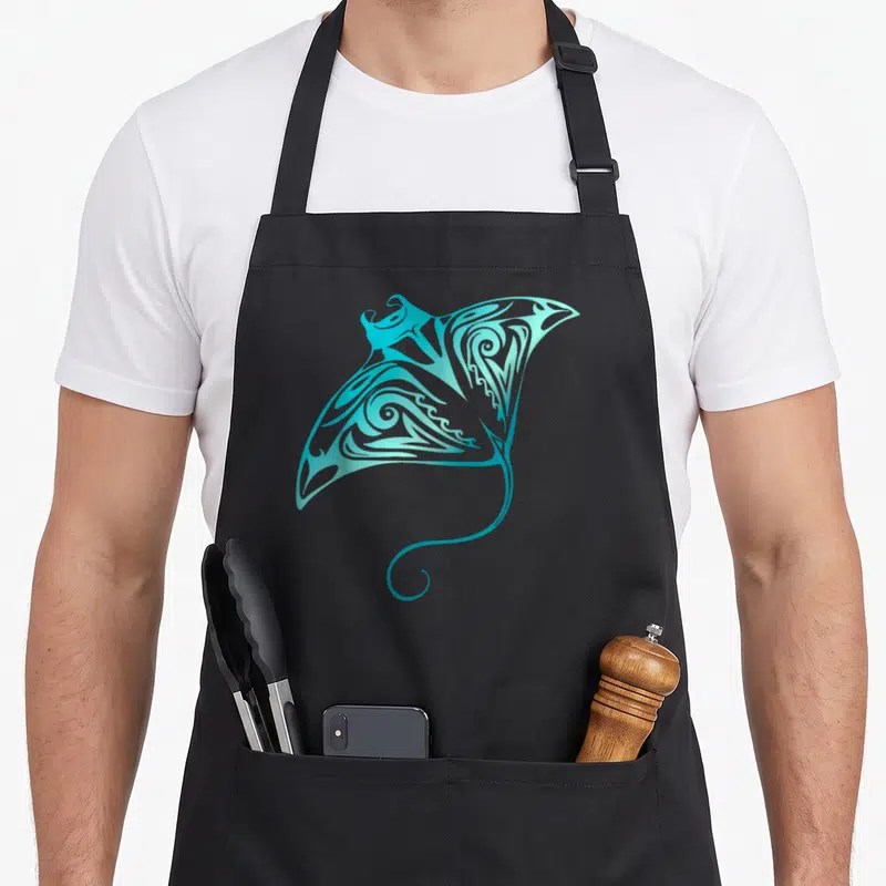 Tablier de cuisine noir avec une raie manta tribale turquoise aux motifs spirales complexes.