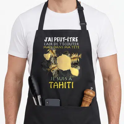 Tablier de cuisine noir avec carte de Tahiti dorée, palmes et phrase humoristique sur fond gris.