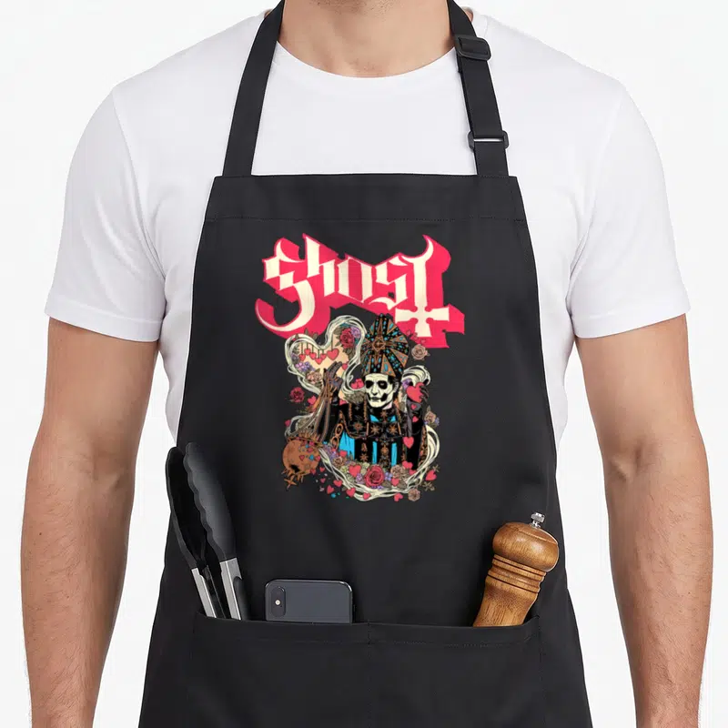 Tablier de cuisine noir avec illustration gothique d'un personnage squelettique en tenue épiscopale entouré de cœurs roses et de roses.