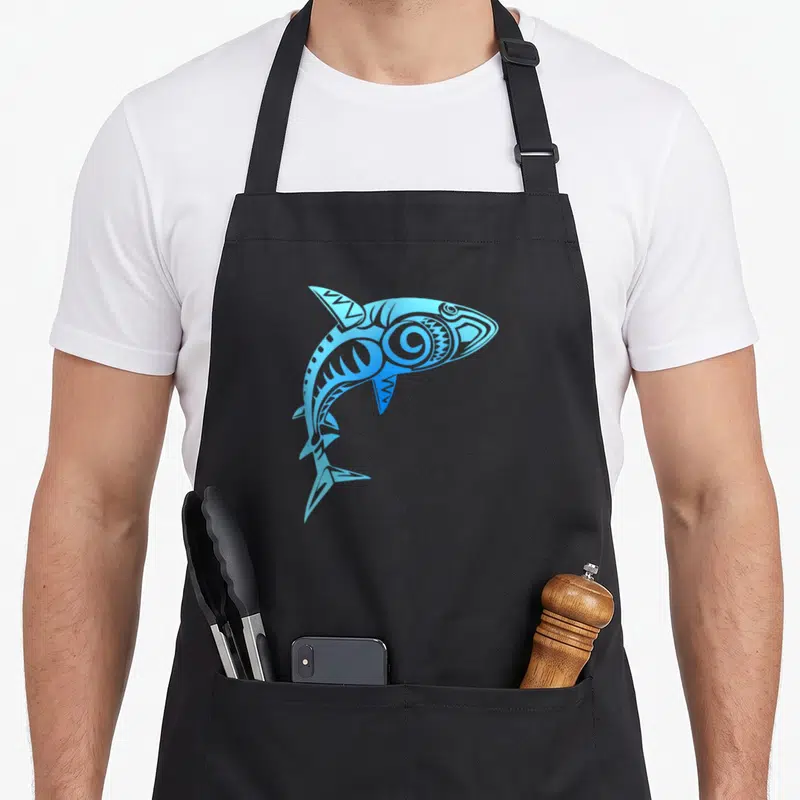 Tablier de cuisine noir avec un grand requin tribal bleu Hawaii Mano au design graphique stylisé.