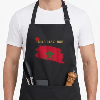 Tablier de cuisine noir avec une brosse de drapeau marocain, une fez rouge et l'inscription Dima Maghrib en lettres dorées.