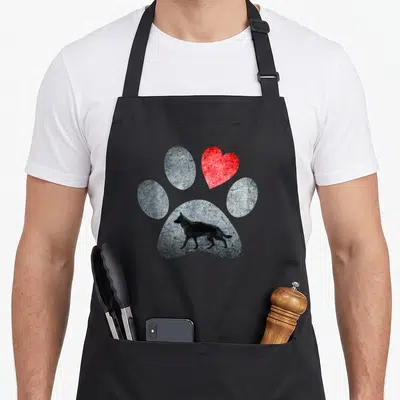 Tablier de cuisine noir avec une patte grise contenant un chien et un cœur rouge texturé.