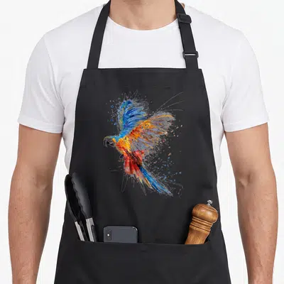 Tablier de cuisine noir avec un perroquet aux ailes déployées peint en bleu, orange et rouge avec des éclats artistiques.