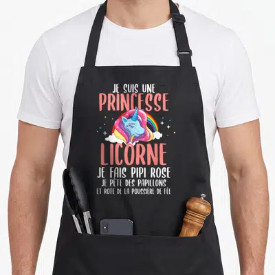 Tablier de cuisine noir avec une illustration de licorne bleue aux cheveux roses et des textes humoristiques sur fond blanc.