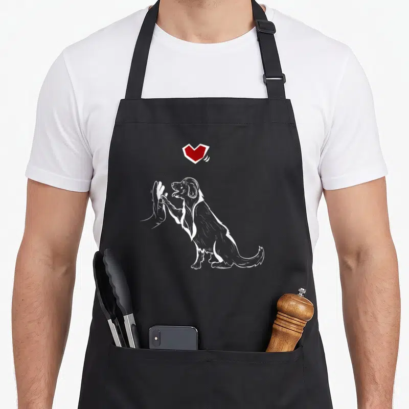 Tablier de cuisine noir avec illustration blanche d'un chien faisant un high five sous un cœur rouge vif.